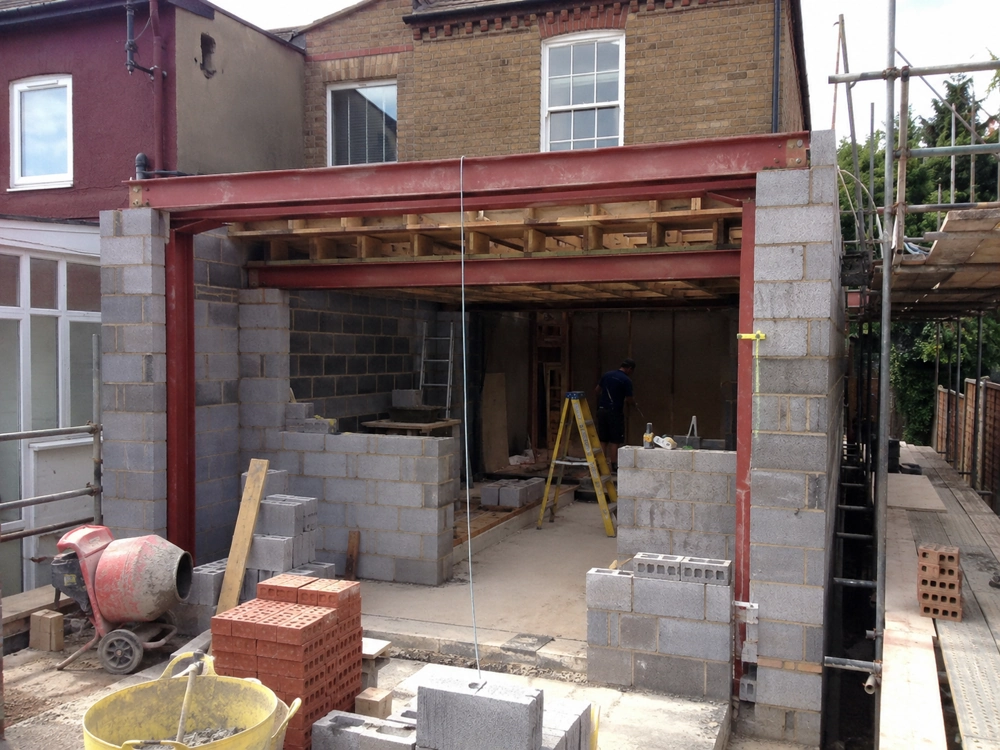 Partially built single storey extension with blockwork walls, exposed steel beams and construction tools