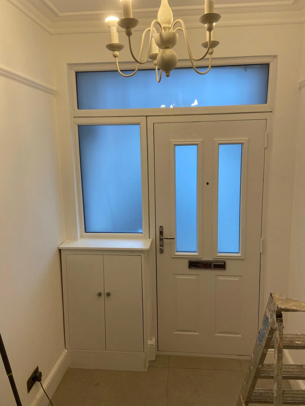 Entrance hallway after Home Renovation with tiled floor, painted walls, fitted door, built-in cabinet and chandelier
