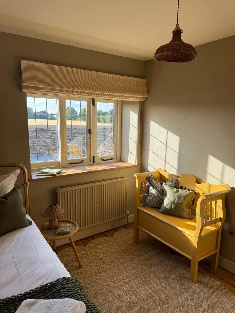Renovated bedroom corner featuring bespoke furniture wooden storage bench under window, radiator, wood flooring and neutral painted walls