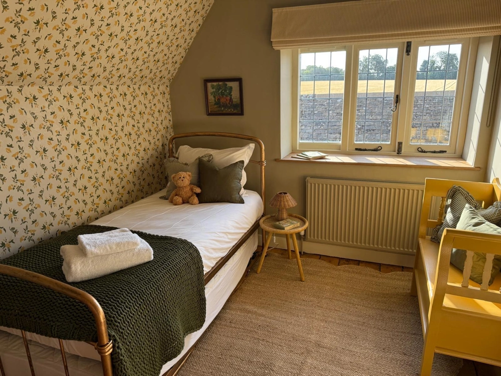 Cosy attic bedroom with timber flooring, floral wallpapered sloped wall, single bed with knitted throw and window, Attic Conversion