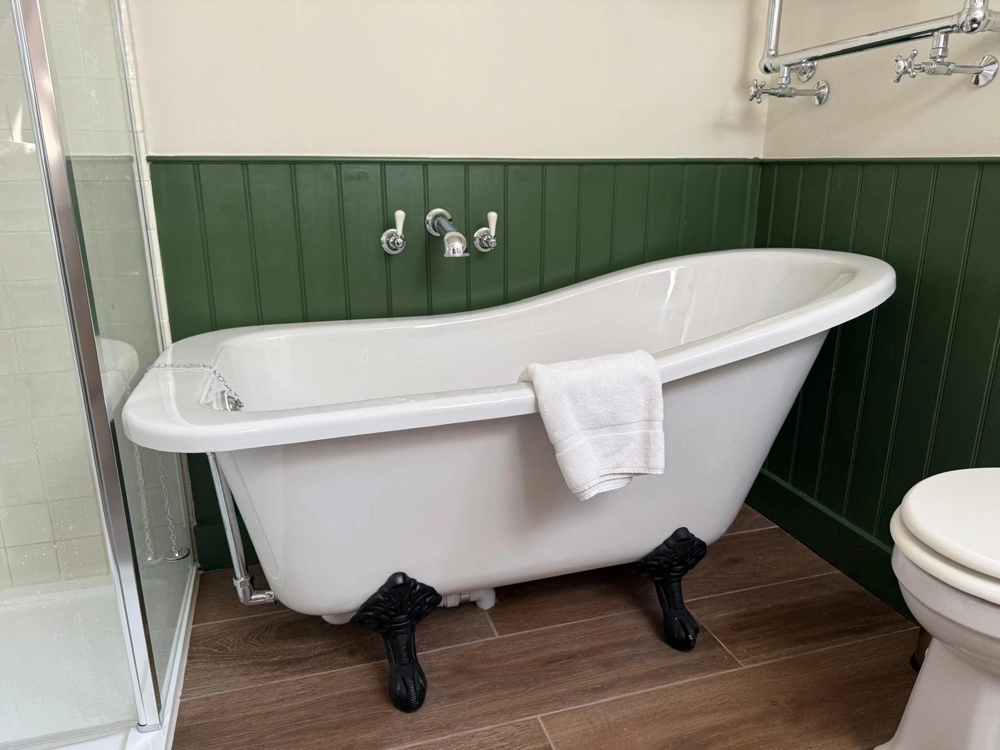 Freestanding clawfoot bathtub with white towel in renovated bathroom with green paneling and wood-look floor tiles Bathroom Installation