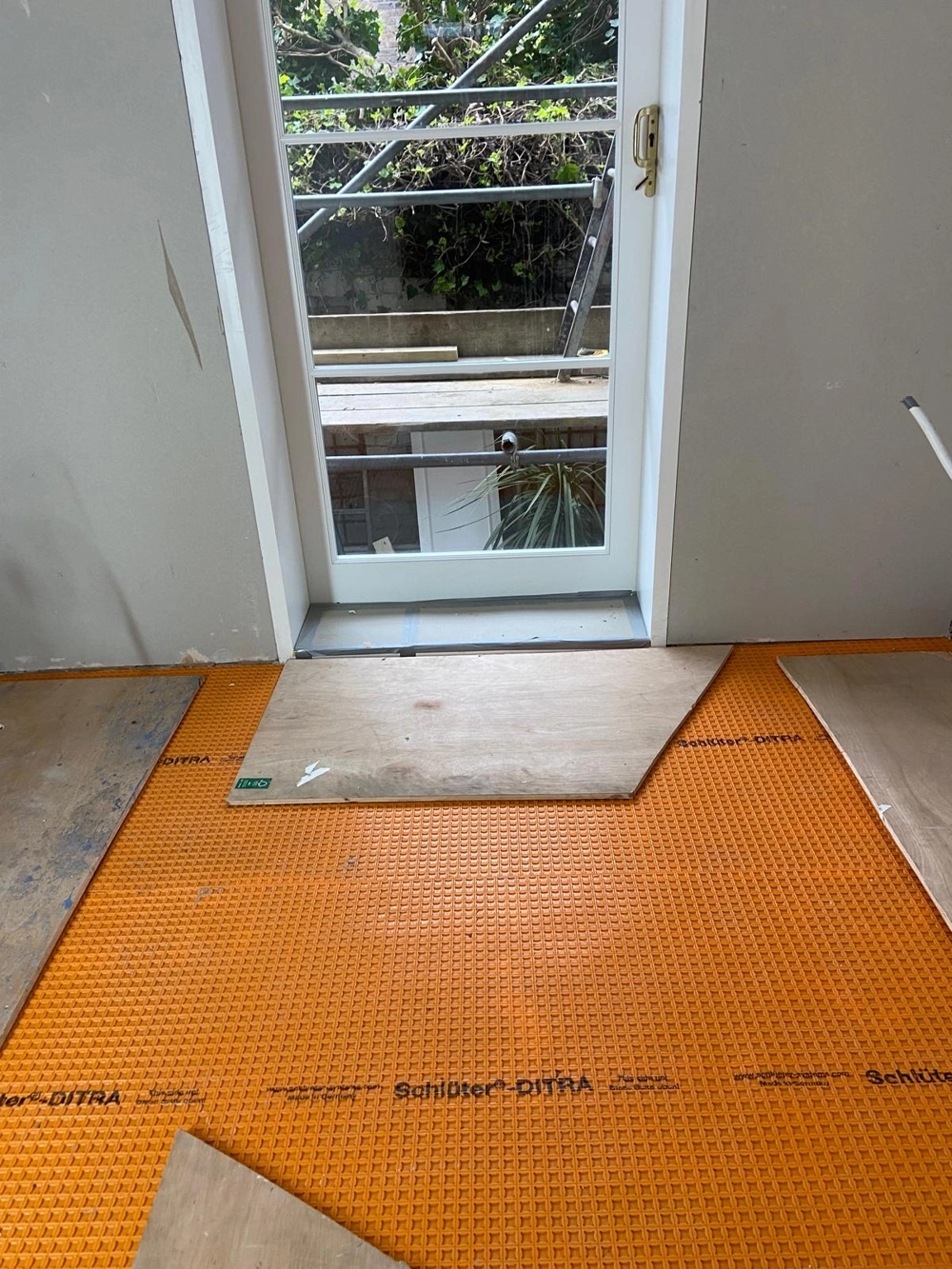 Orange uncoupling membrane laid on subfloor with plywood boards under an open door, ready for Floor Tiling