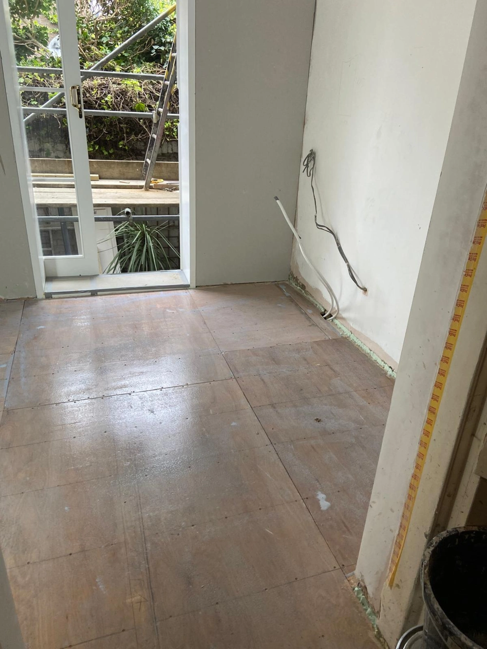 Plywood subfloor prepared for Flooring Installation in renovated room with exposed wiring and open patio doors
