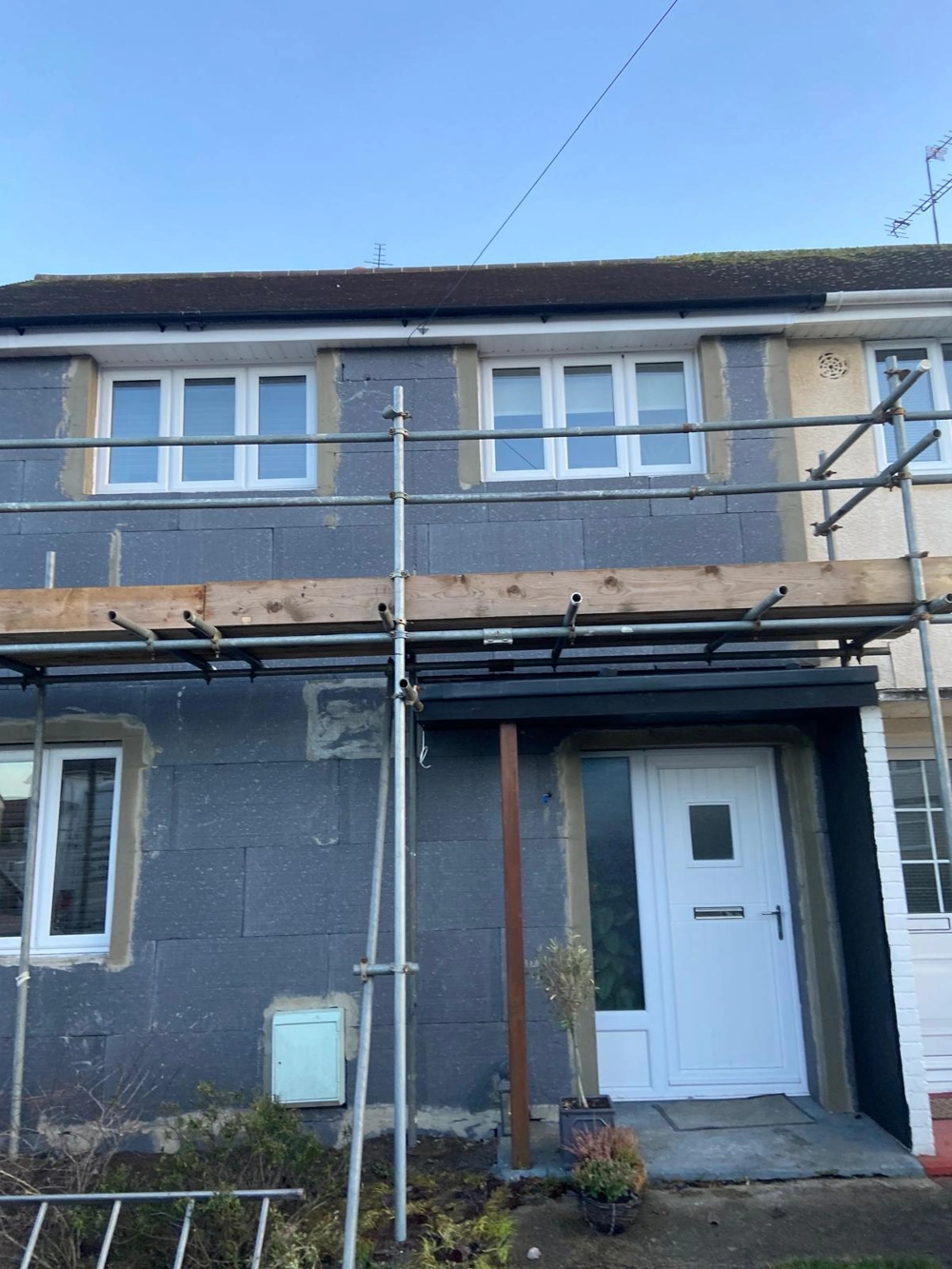 Front elevation of a terraced house with insulation boards and scaffolding for Rendering service