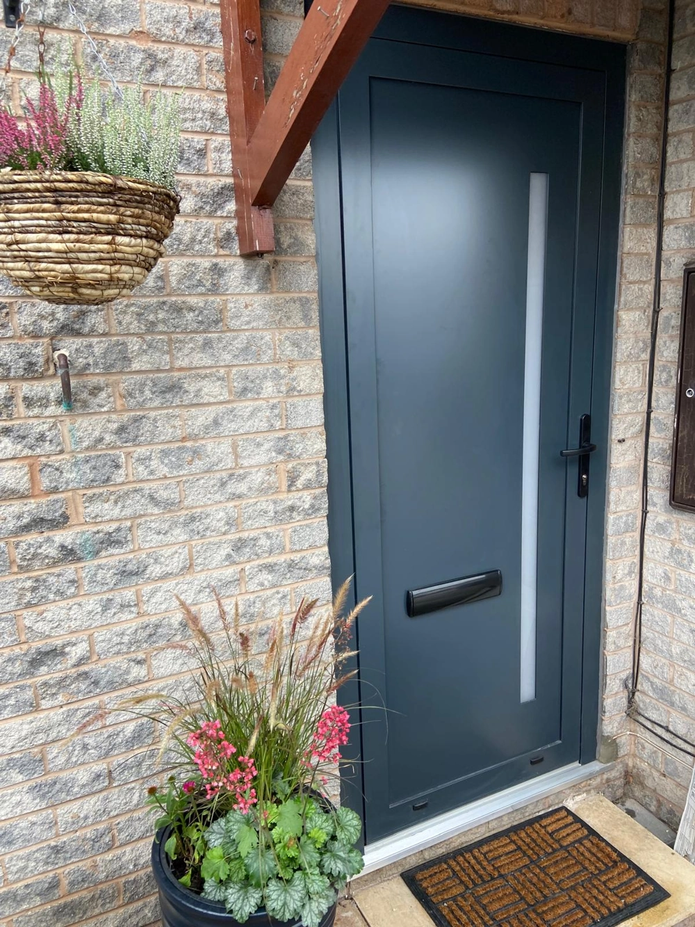 Dark grey modern front entrance door with vertical frosted glass and brick surround, potted plants