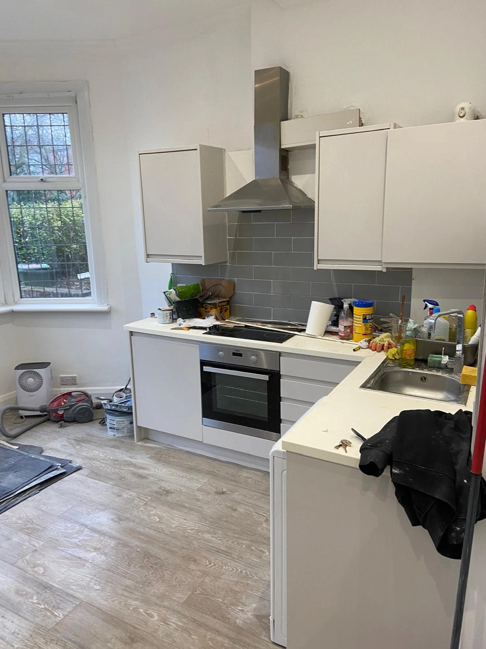 Partially installed white kitchen cabinets with new wooden flooring and gray subway tile backsplash during kitchen fitting