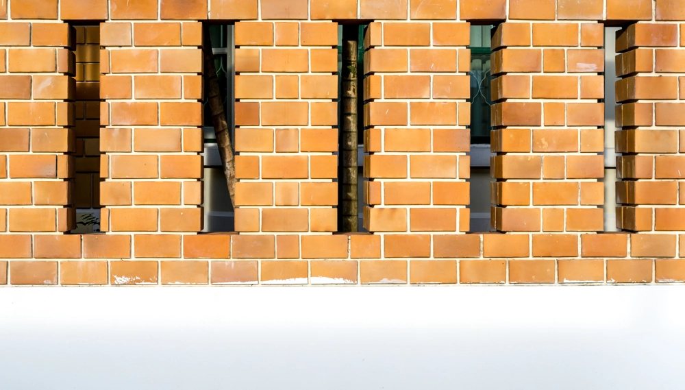 Bricklaying: red brick exterior wall with vertical slits revealing window frames behind