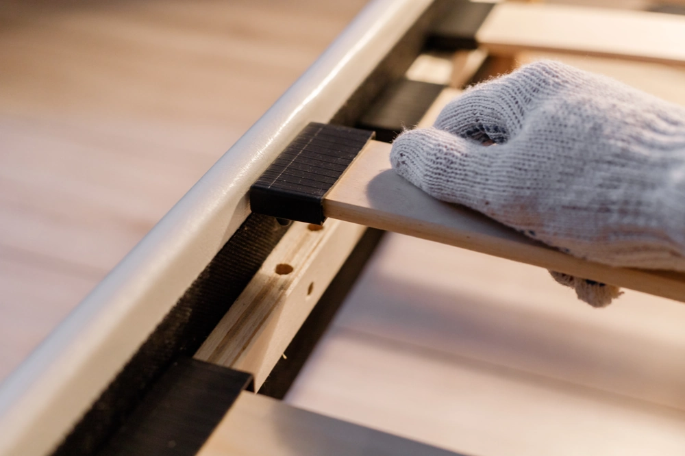 Gloved hand assembling wooden slats into a metal frame during carpentry work