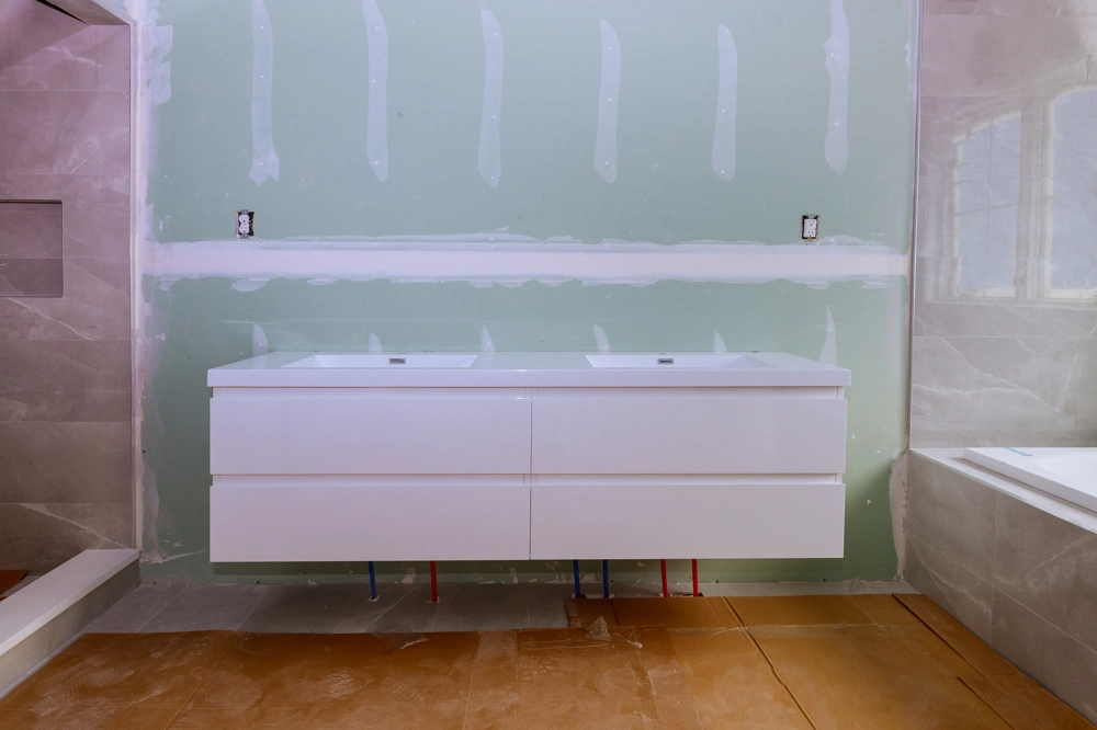 Floating double vanity installed on primed drywall with exposed pipes during Bathroom Renovation