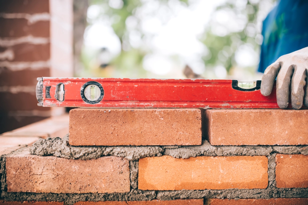 Gloved hand holding a spirit level on a freshly built brick wall during Bricklaying