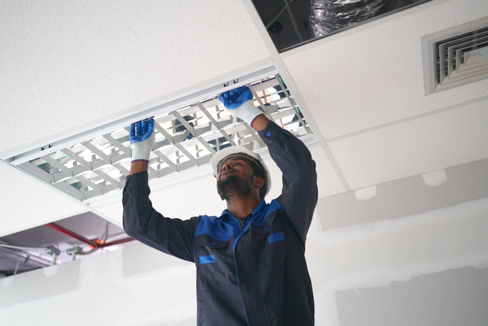 Construction worker in hard hat fitting a suspended ceiling grid in interior space for Suspended Ceiling service
