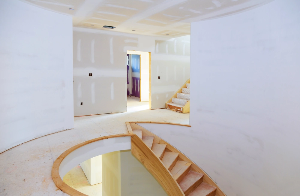 Upper-level interior renovation with drywall partitions and curved wooden staircase Drylining