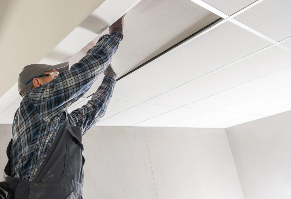 Worker fitting white suspended ceiling tiles during interior renovation