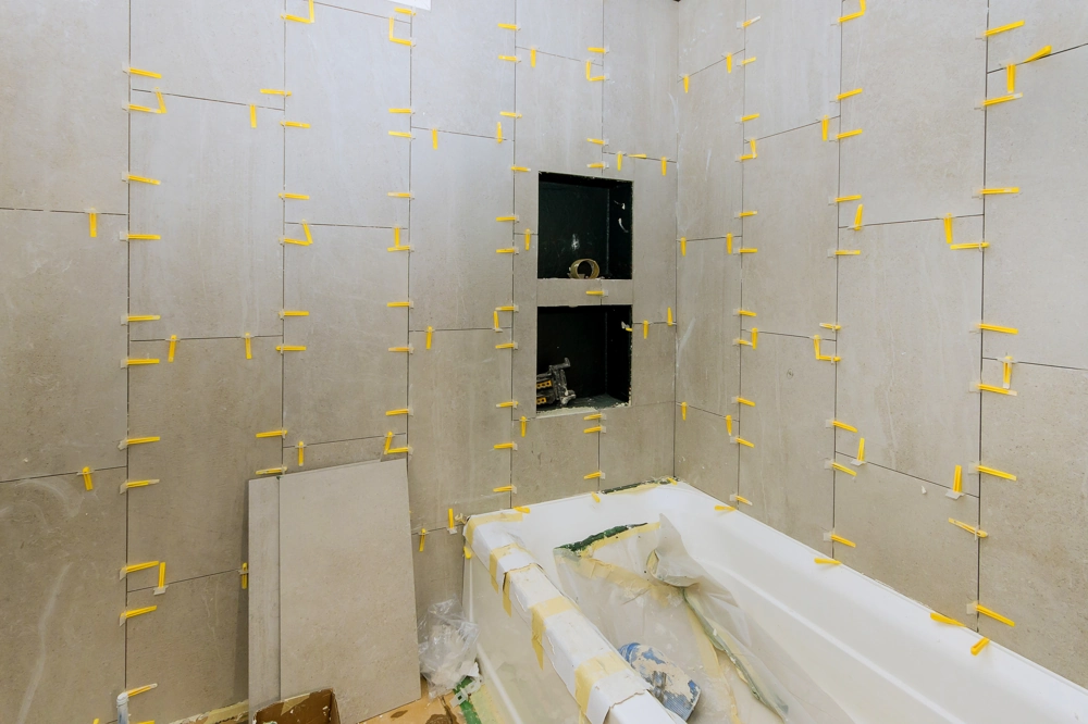 Bathroom Tiling in-progress with spacers on large wall tiles and protective wrapping on bathtub