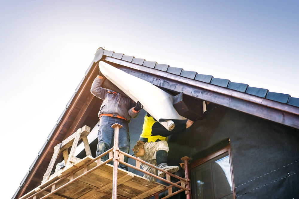Two workers on scaffolding installing roof underlay beneath eaves Roofing