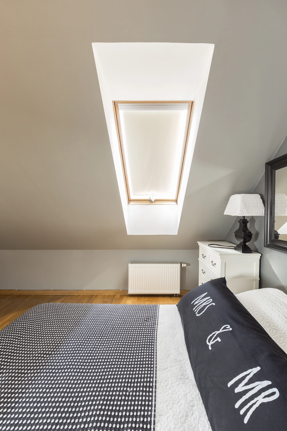 Attic bedroom with roof window, wood flooring, radiator and bedside table illustrating Loft Conversion
