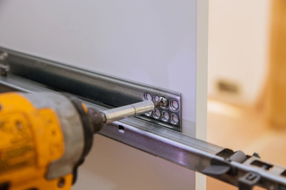 Carpentry installation of metal drawer slide bracket on cabinet panel
