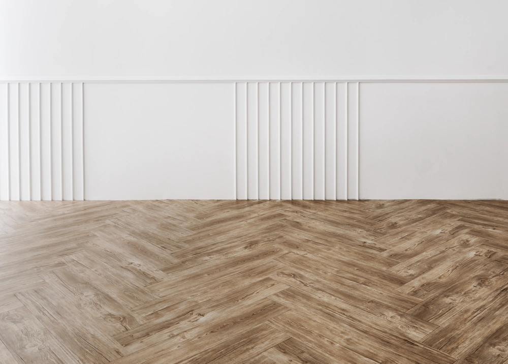 Empty interior showcasing herringbone Wood Flooring against a white decorative panelled wall