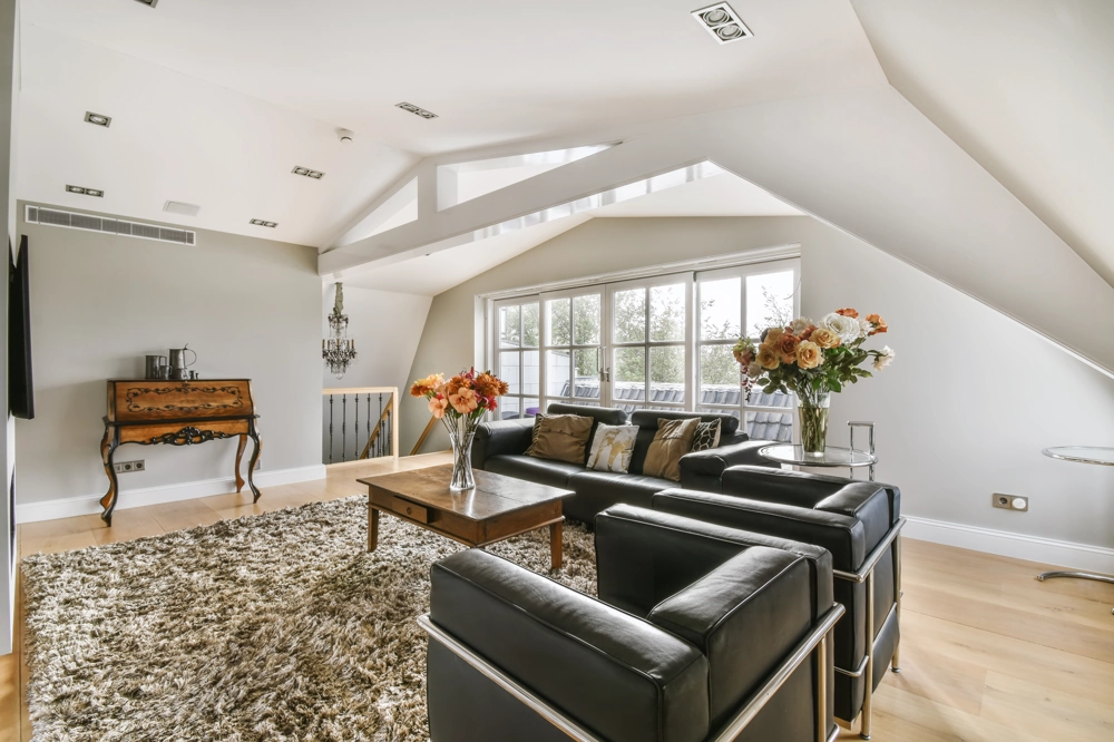 Converted attic living room after Attic Conversion featuring black leather sofas, wooden coffee table and shag rug