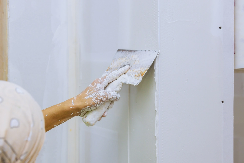 Close-up of hand smoothing white plaster on an interior wall with spatula, illustrating Plastering service