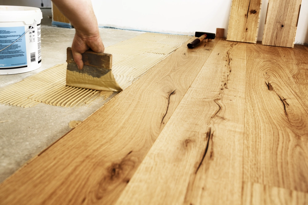 Spreading adhesive with a trowel and fitting oak floorboards for Wood Flooring