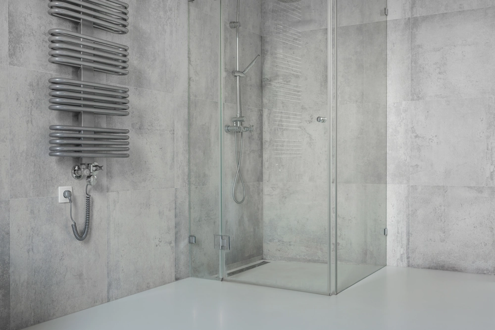 Glass shower enclosure with grey tiled walls, white floor and wall-mounted radiator – Shower Installation