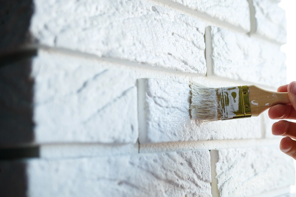 Hand painting a brick wall with white paint using brush as part of Exterior Painting service