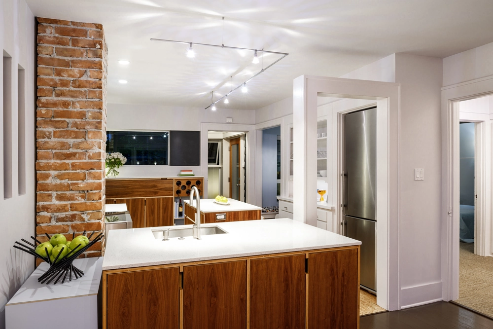 Modern kitchen renovation with white quartz island countertop, wooden cabinets and exposed brick column