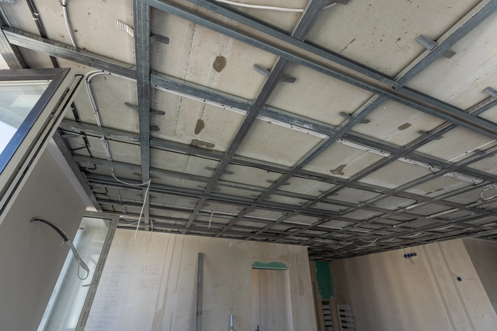 Suspended ceiling installation with metal grid and exposed electrical wiring against unfinished plastered walls