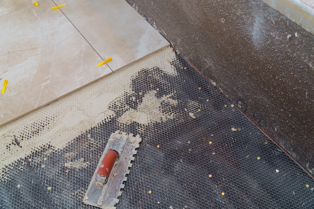 Floor tiling in progress with ceramic tiles on mesh underlayment, thinset mortar, spacers and notched trowel
