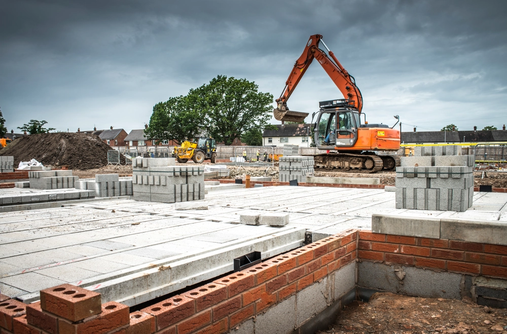 Excavator on construction site with concrete foundation and stacked blocks for blockwork