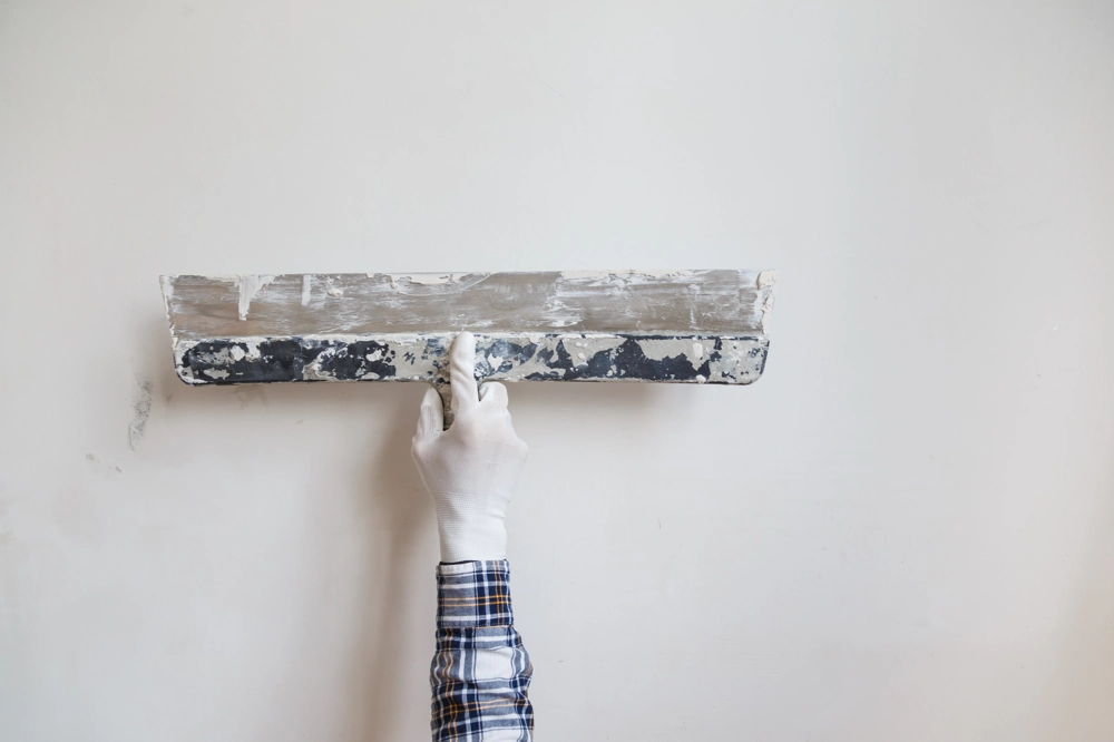 Gloved hand applying and smoothing plaster on a white wall with a metal float – Plastering
